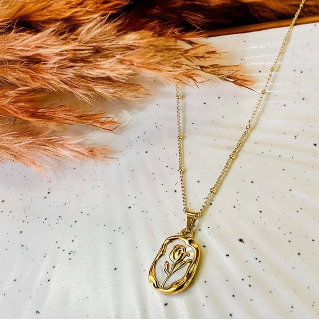 Gold necklace with a tulip pendant on a white surface with dried orange leaves.
