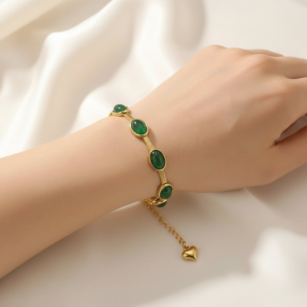 Gold bracelet with green gemstones on a wrist against a white background