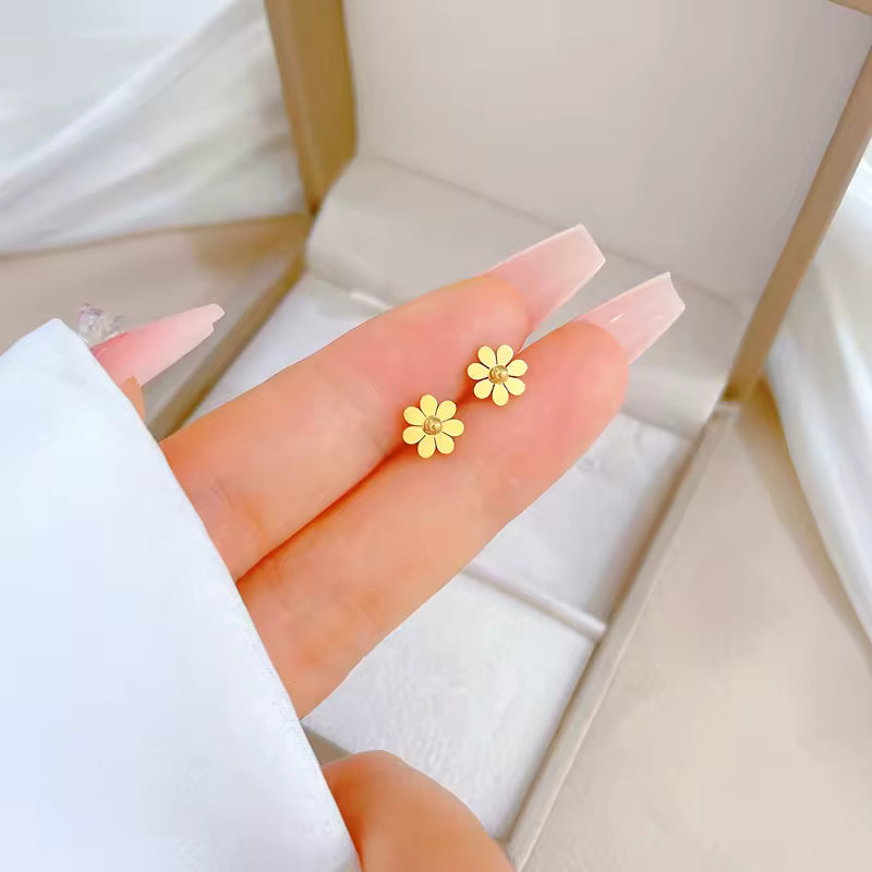 Gold flower-shaped earrings held between fingers with a white background