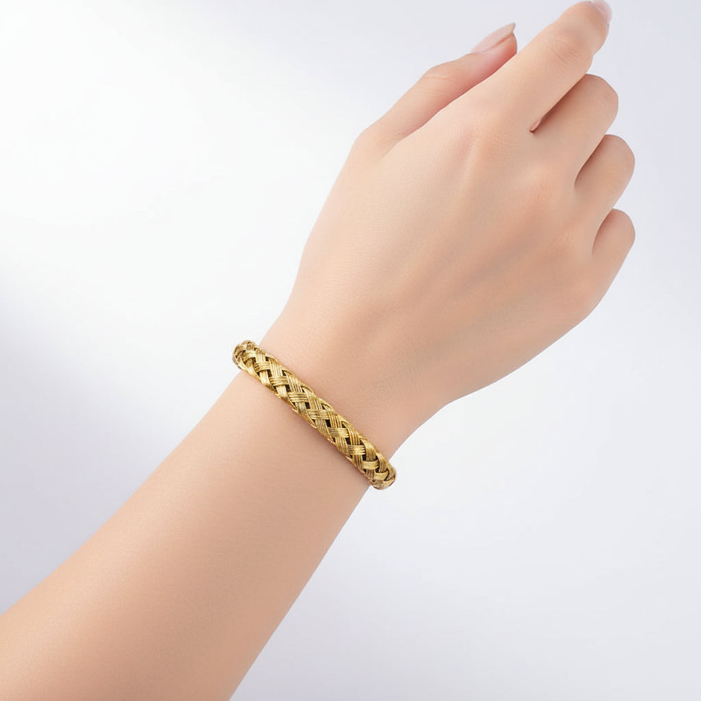 A gold braided cuff bracelet displayed on a gray jewelry box.