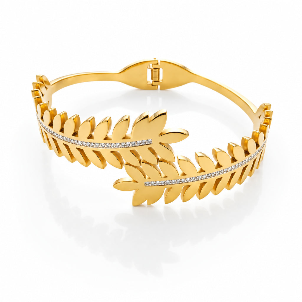A gold bangle bracelet featuring a leafy design with a central row of small clear stones, displayed on a clean white background.