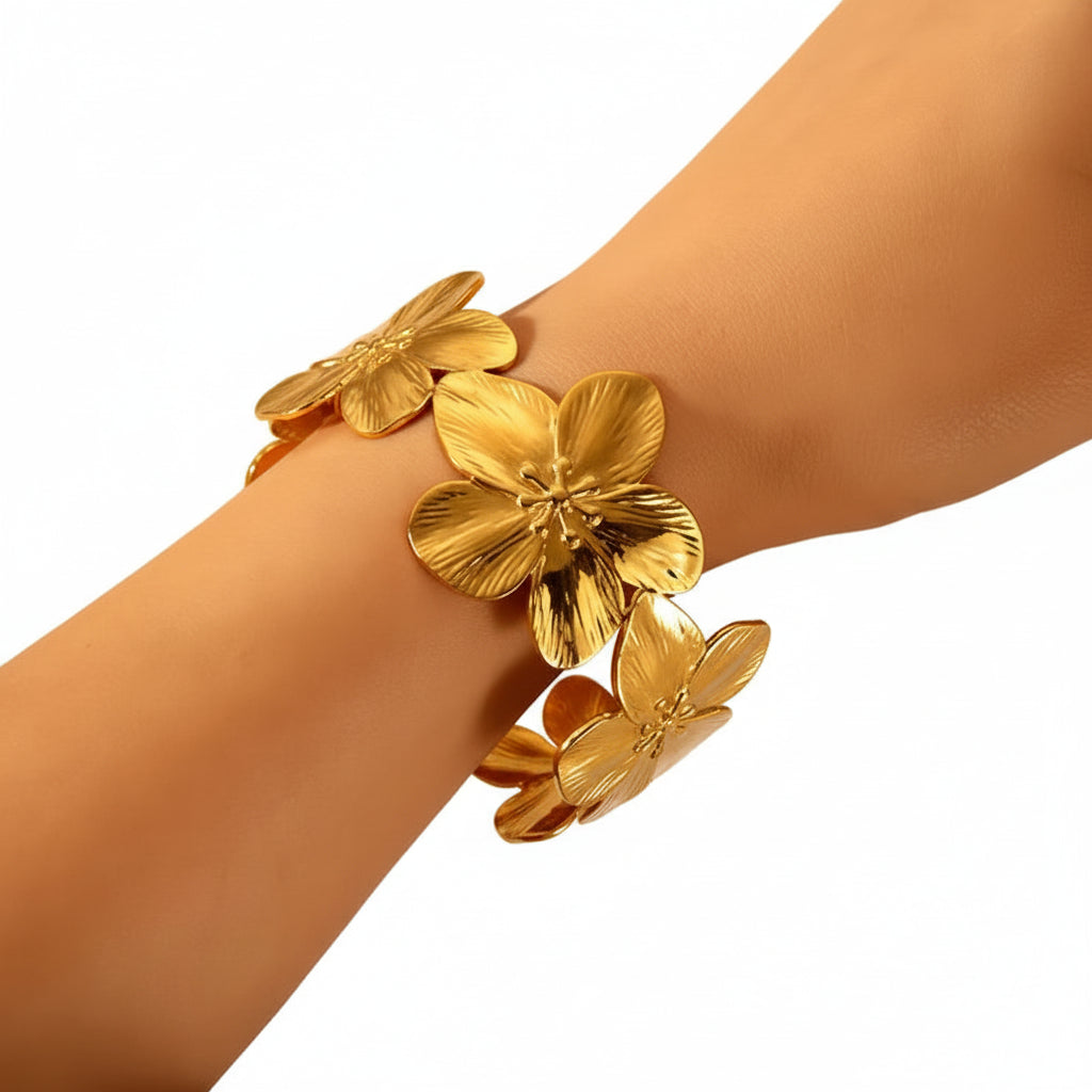 A close-up of a gold-tone floral cuff bracelet worn on a person's wrist, featuring three large textured flower petals and a warm orange-red inner band.