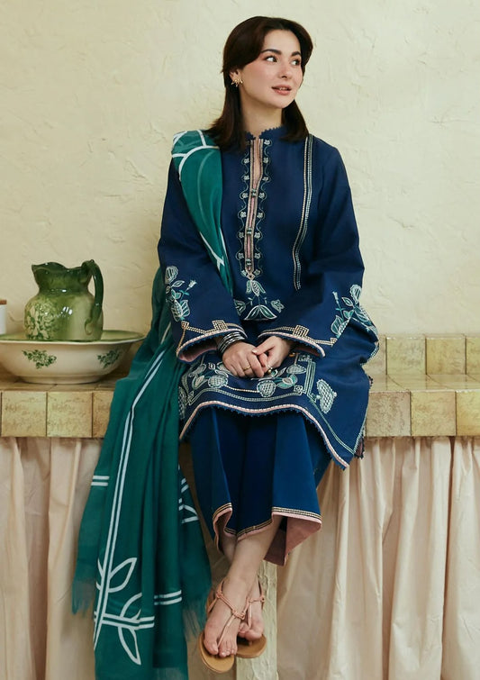 Person wearing a blue embroidered outfit with a green dupatta sitting on a bench.