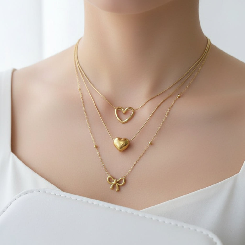 Three gold necklaces with heart and bow pendants on a white surface