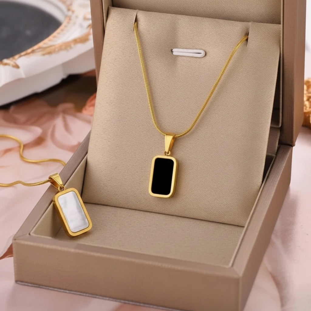 Gold rectangular pendant necklace with a black center, displayed in a beige jewelry box with an inset close-up of the pendant.