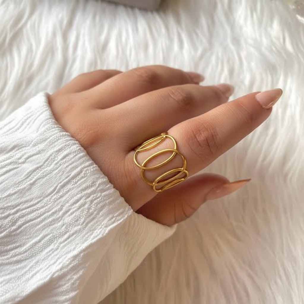 A close-up of a hand wearing a gold open-link ring, resting on a white faux fur surface.