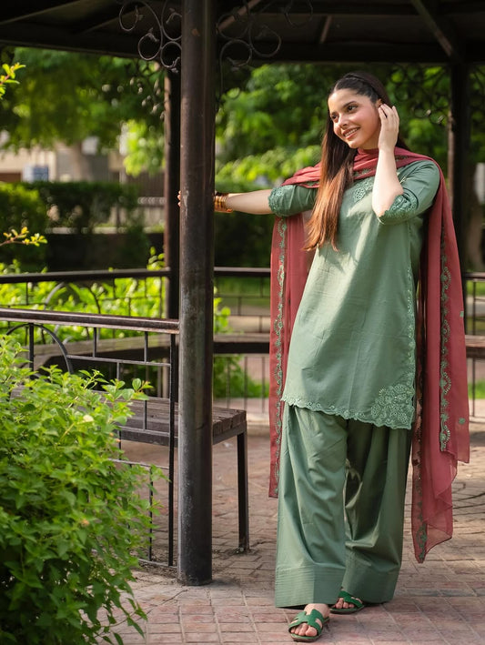 Woman in green traditional outfit with a red dupatta standing outdoors.