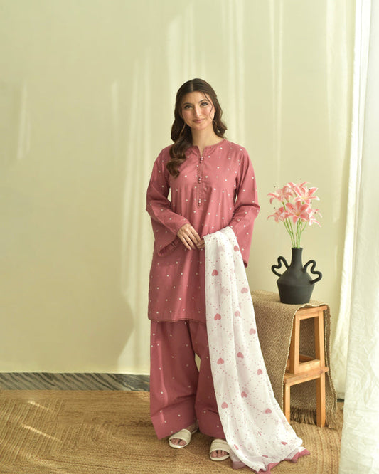 Woman in a pink traditional outfit with a white scarf in a room with a vase and flowers.