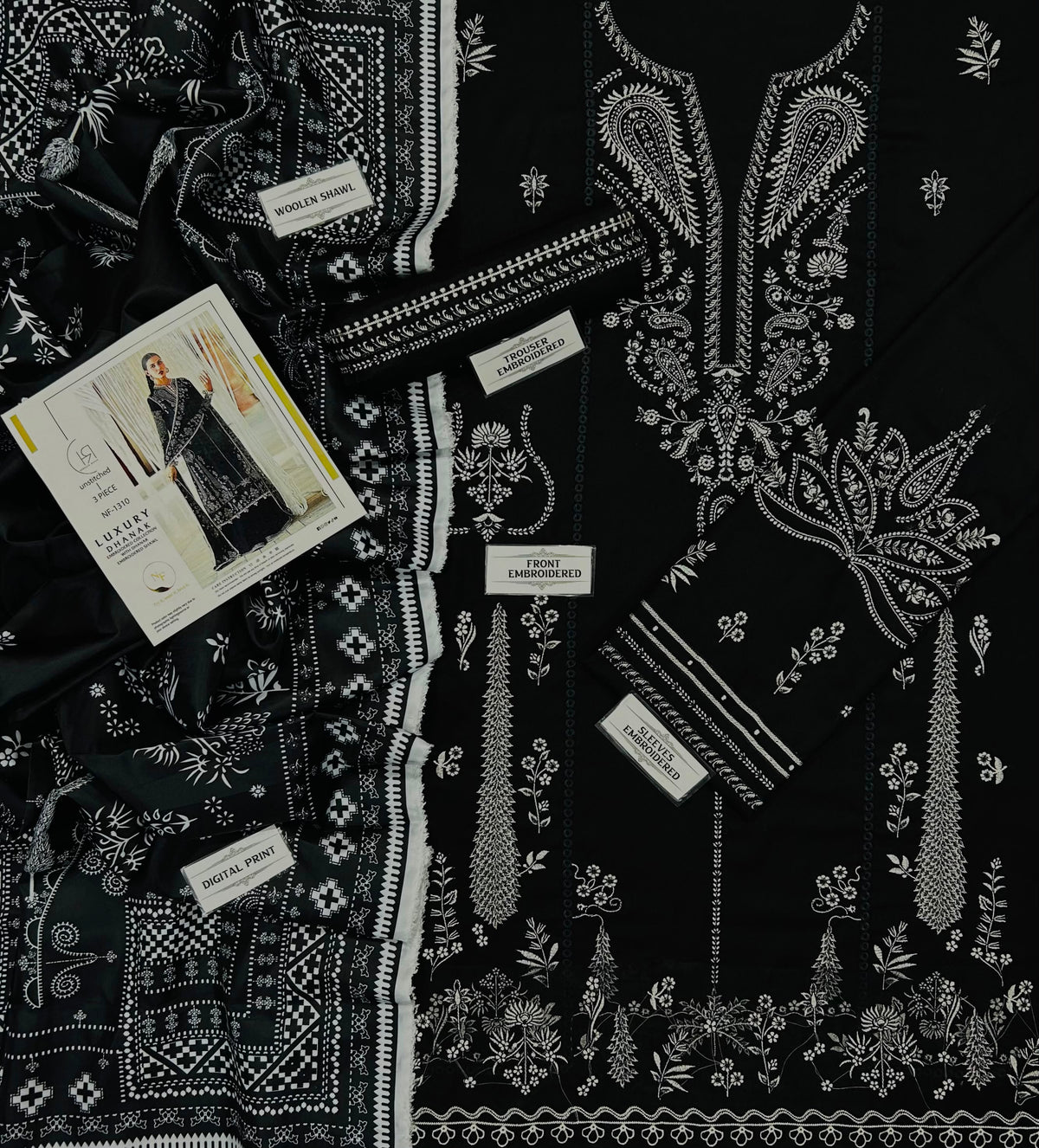 Black cotton fabric with intricate white embroidery, shown in a flat-lay arrangement alongside a matching printed fashion magazine and several fabric labels.