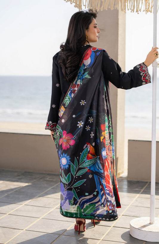 Woman wearing a colorful floral abaya with a black background, standing on a rooftop with ocean view.