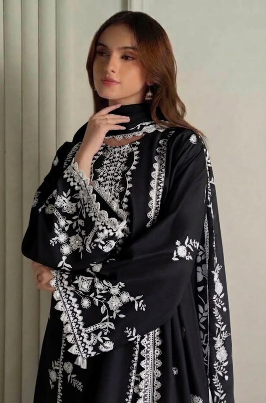 A woman wearing a black embroidered tunic with white floral and geometric patterns, posed against a neutral light beige background.