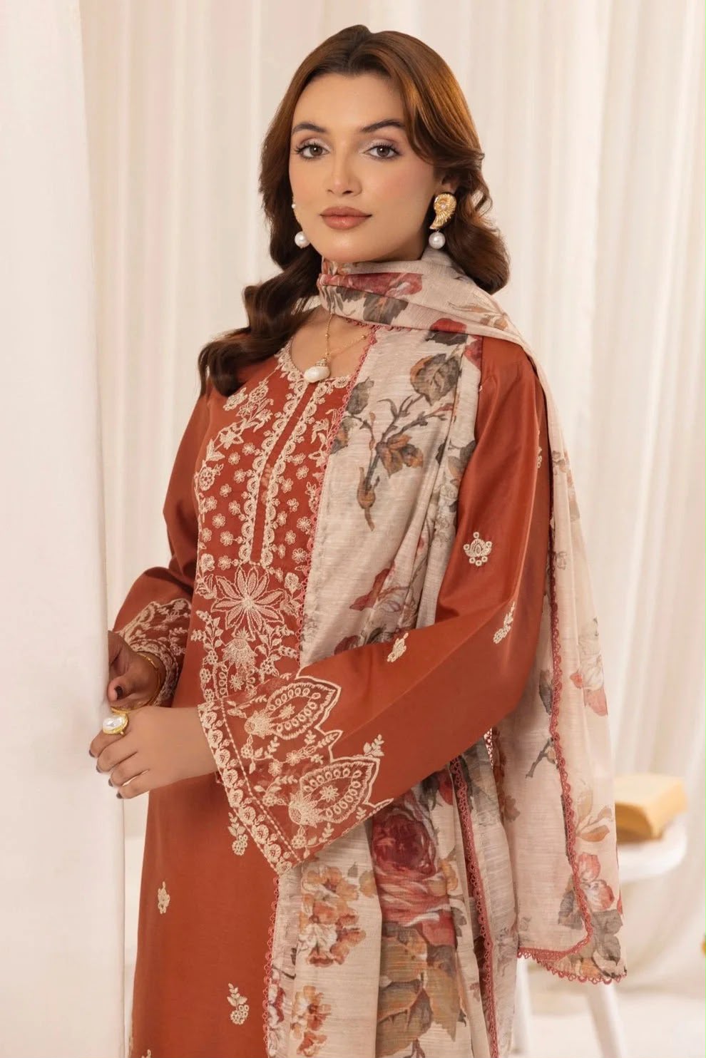 Woman wearing a traditional outfit with a patterned dupatta against a white curtain background