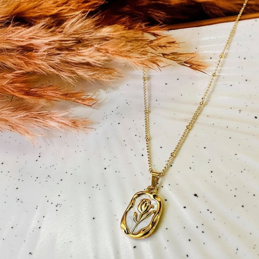Gold necklace with a tulip pendant on a white surface with dried orange leaves.