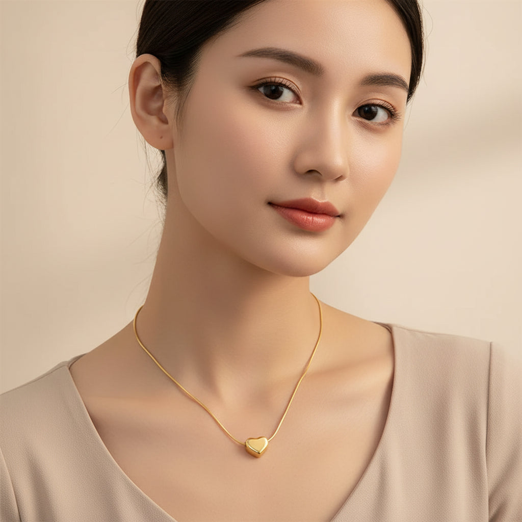 A gold heart-shaped pendant necklace with a delicate chain and an adjustable lobster clasp, displayed on a soft beige satin fabric background.