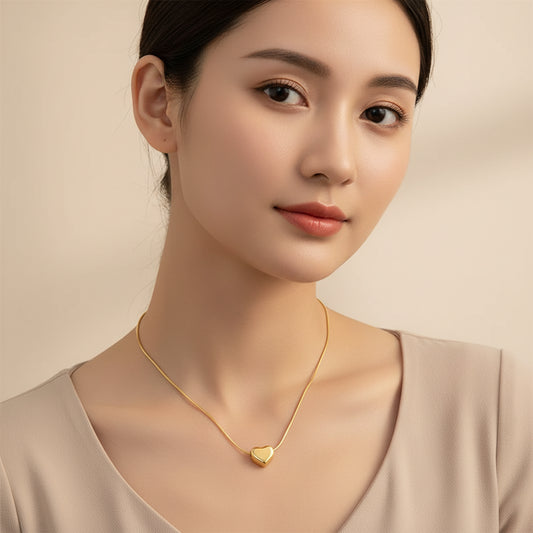 A gold heart-shaped pendant necklace with a delicate chain and an adjustable lobster clasp, displayed on a soft beige satin fabric background.
