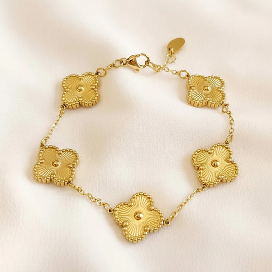 A gold-tone bracelet featuring five textured, flower-like oval links connected by a delicate chain, displayed on a soft, light beige fabric background.