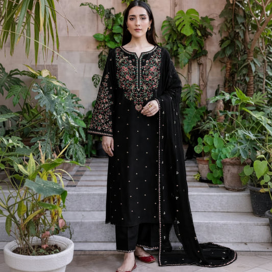 Woman in a black embroidered outfit standing outdoors with plants in the background