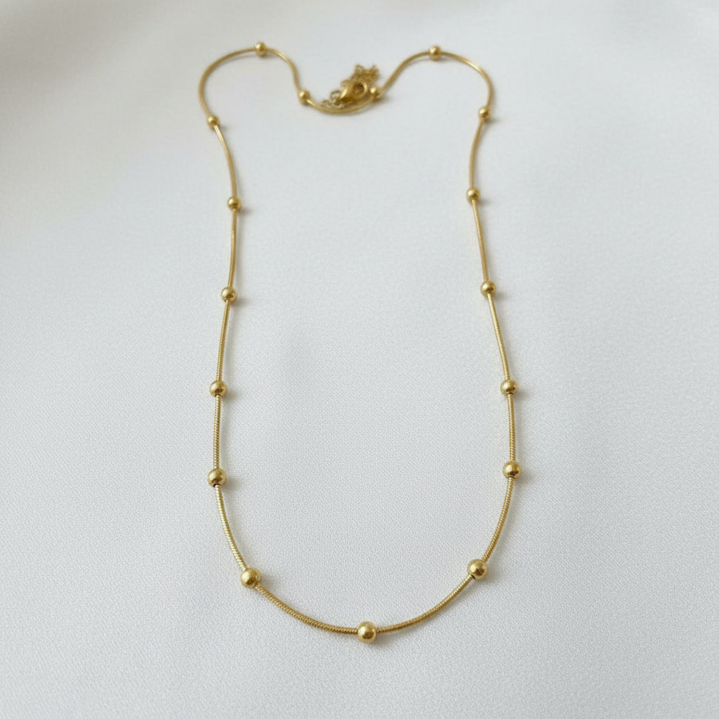 A gold beaded chain necklace laid out on a light beige fabric background.