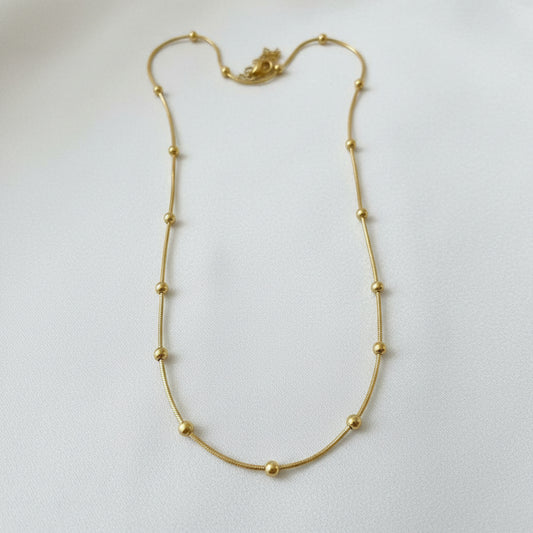A gold beaded chain necklace laid out on a light beige fabric background.