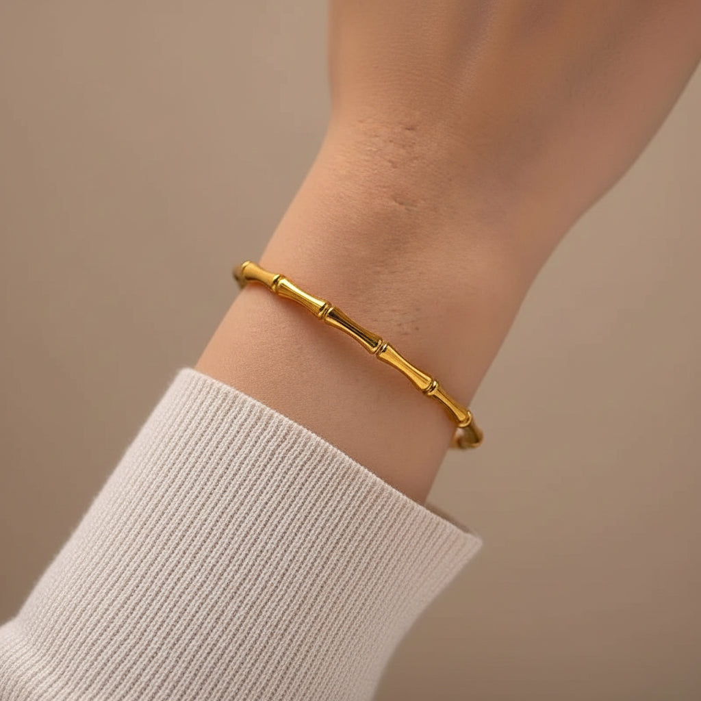 A gold bamboo bracelet worn on a person's wrist, shown in a close-up shot against a soft, light-colored ribbed knit top.