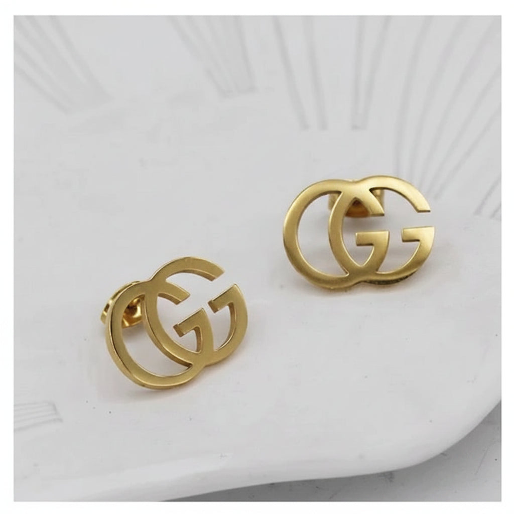 A pair of gold-toned interlocking G earrings with a double-G logo design, displayed on a white textured ceramic plate.
