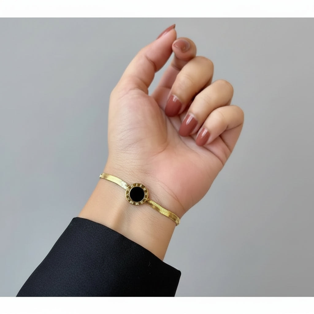 Gold bracelet with a black stone on a wrist against a neutral background