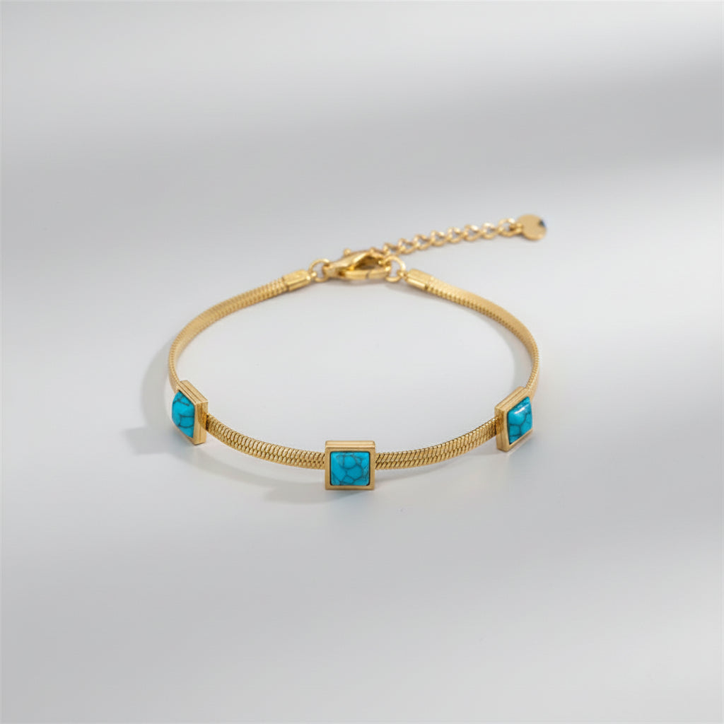 Gold bracelet with turquoise stones on a wrist against a white background