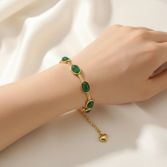 Gold bracelet with green gemstones on a wrist against a white background