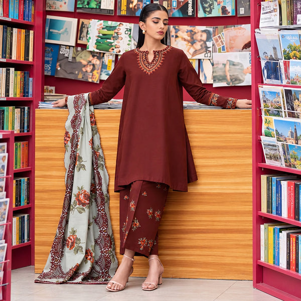 Woman in a brown traditional outfit standing in front of a wooden counter with a colorful background.