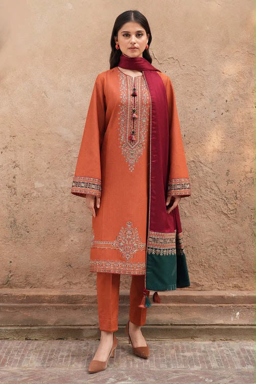 Woman wearing an orange embroidered outfit with a red dupatta against a beige wall.
