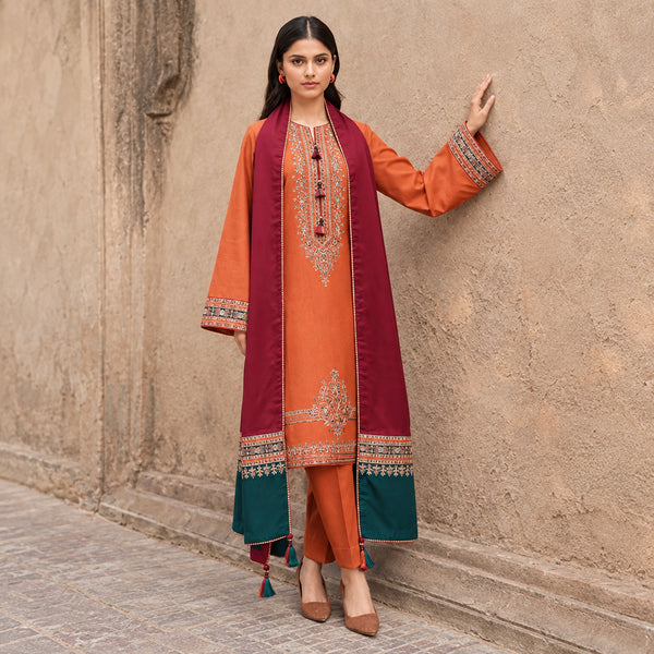 Woman wearing an orange and red embroidered traditional outfit against a stone wall.