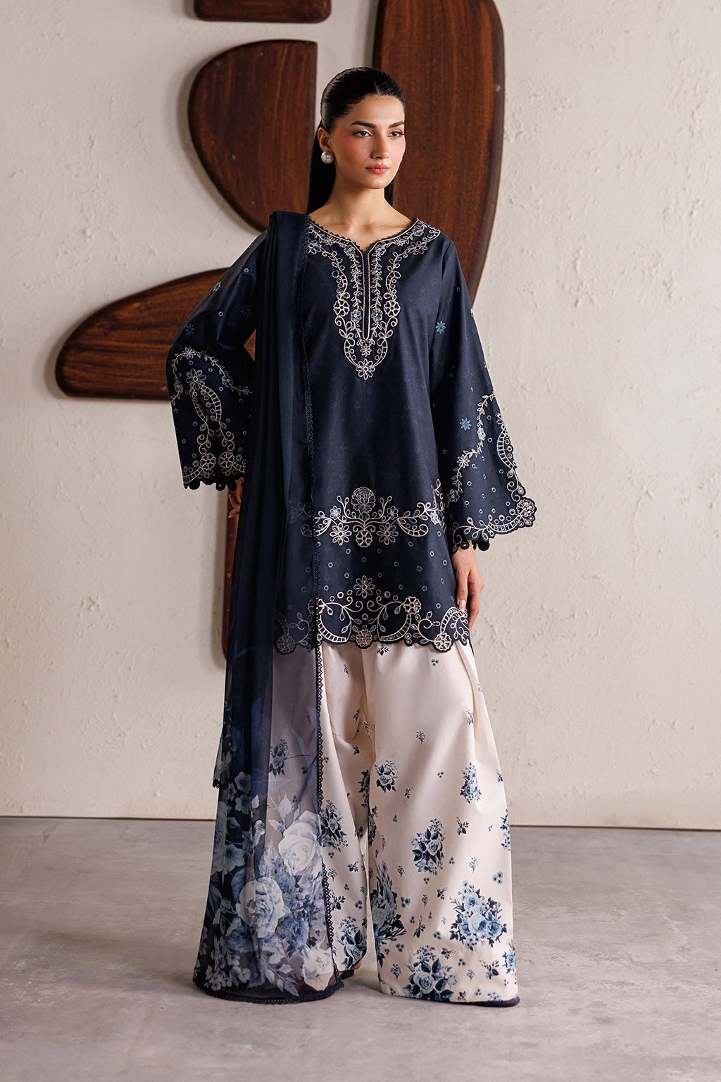 Woman wearing a navy blue embroidered top and white palazzo pants with floral patterns.