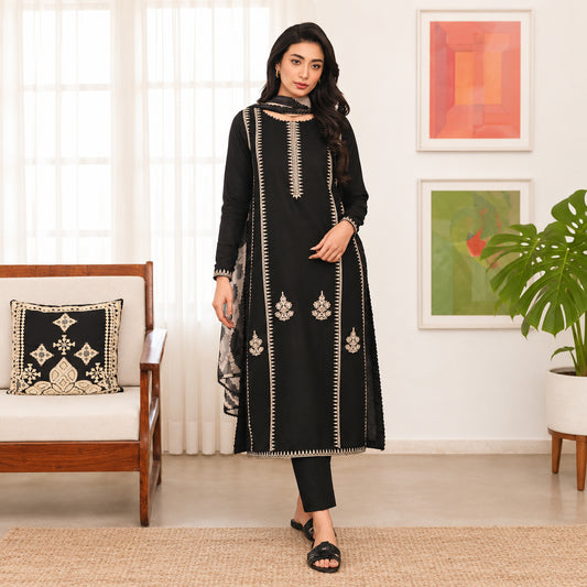 Woman in a black embroidered outfit standing in a living room.