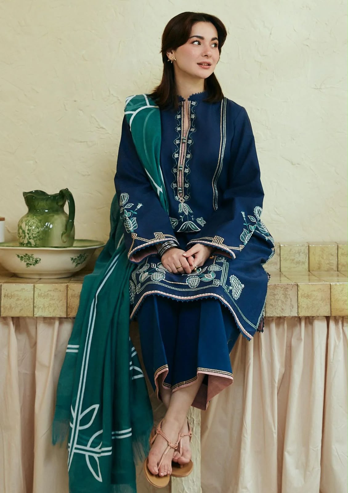 Person wearing a blue embroidered outfit with a green dupatta sitting on a bench.