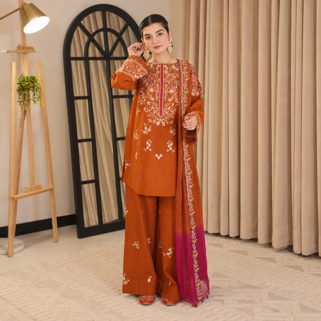 Woman wearing an orange embroidered outfit in a room with beige curtains and a plant.