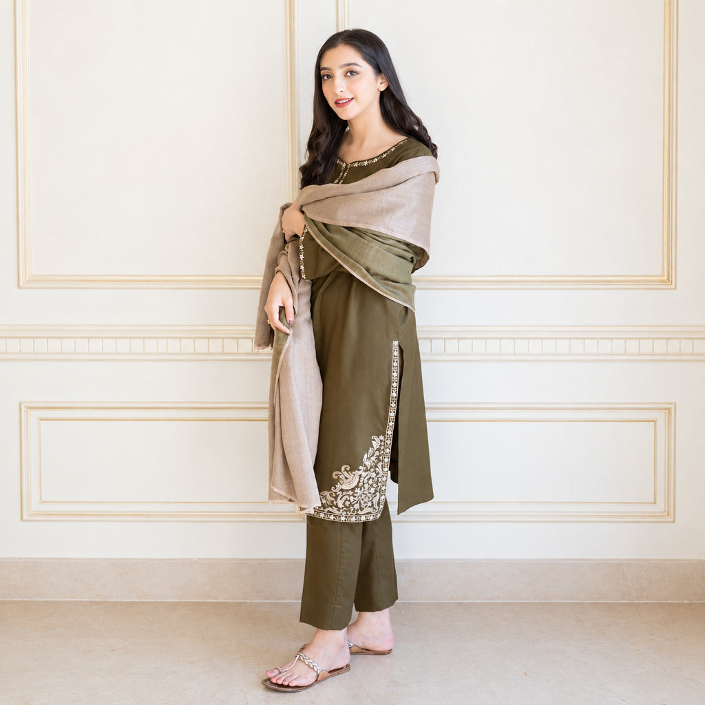 Woman wearing a traditional outfit with a green and beige shawl against a white wall.