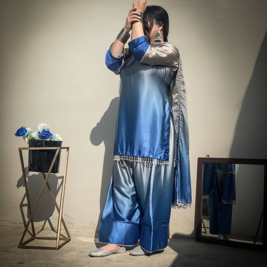 Person wearing a blue and gray traditional outfit with a beige wall background