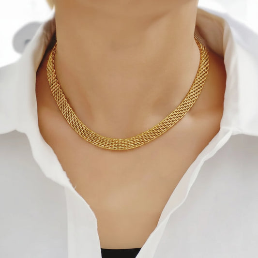 A close-up of a person's neck and collarbone area wearing a thick, woven gold chain necklace over a white collared shirt.