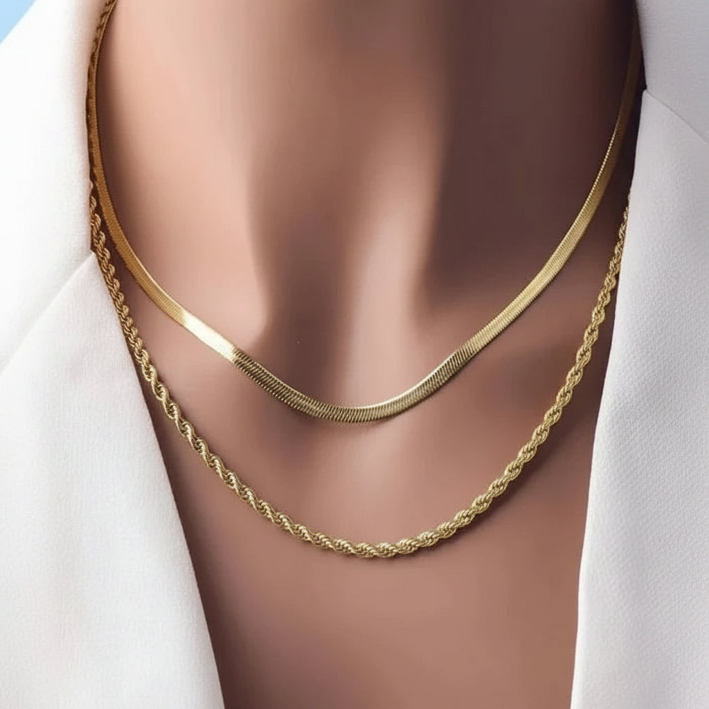 Two gold necklaces, a smooth flat chain and a twisted rope chain, displayed on a mannequin bust wearing a white shirt.