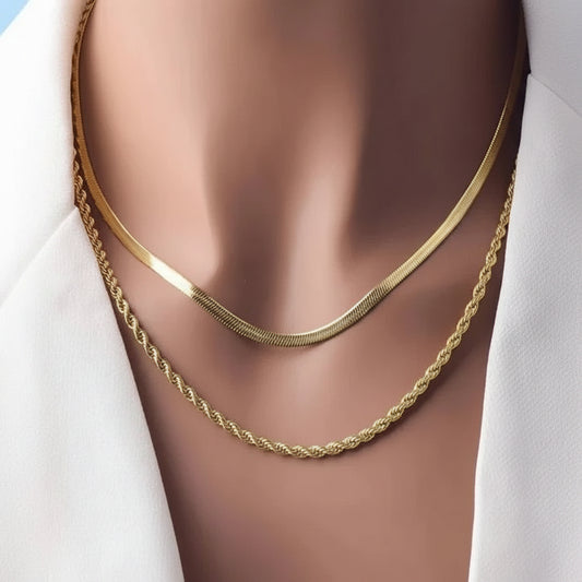 Two gold necklaces, a smooth flat chain and a twisted rope chain, displayed on a mannequin bust wearing a white shirt.