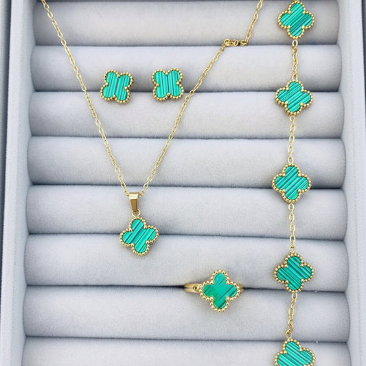 Gold jewelry set with four-leaf clover motifs, including a necklace, ring, and earrings, featuring vibrant turquoise green inlays on a gray display cushion.