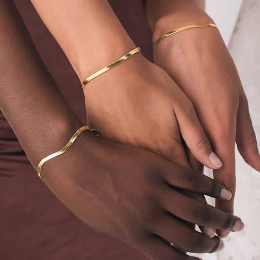 Close-up of hands wearing gold bracelets on a neutral background