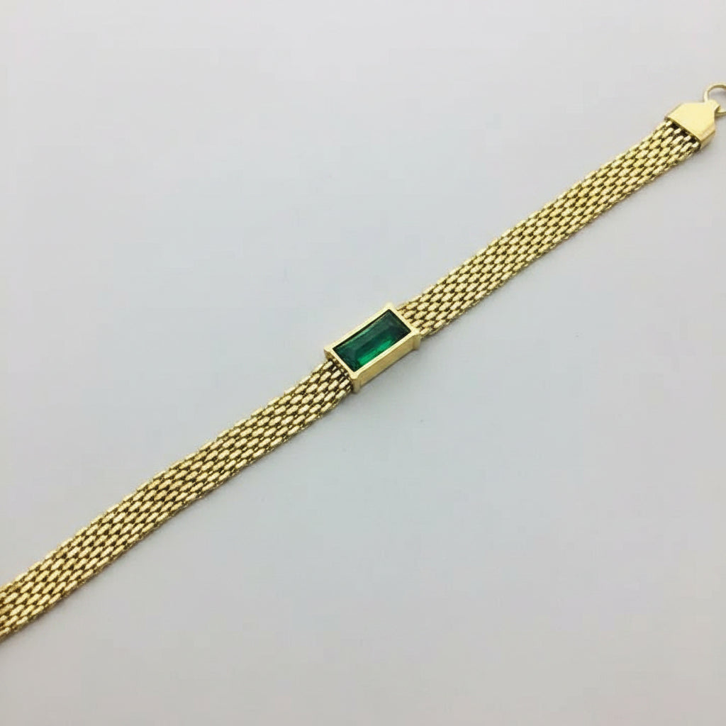 A gold mesh bracelet with a rectangular green stone centerpiece, displayed diagonally on a gray jewelry box.