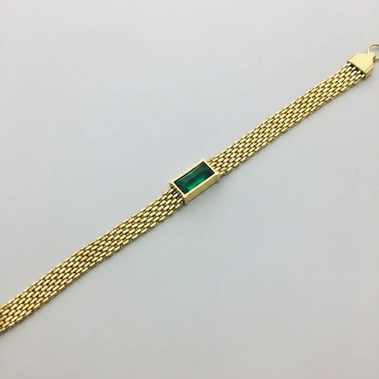 A gold mesh bracelet with a rectangular green stone centerpiece, displayed diagonally on a gray jewelry box.
