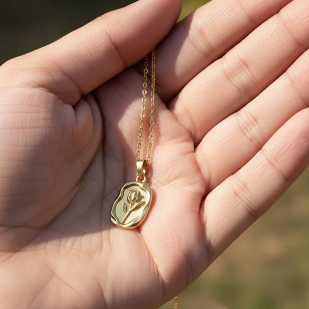 A gold necklace with an irregularly shaped pendant featuring a small floral engraving, held in the palm of a hand.
