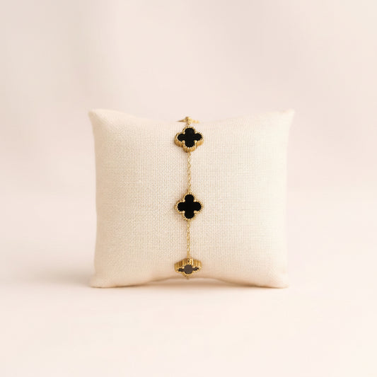 Gold and black clover-shaped bracelet on a beige pillow