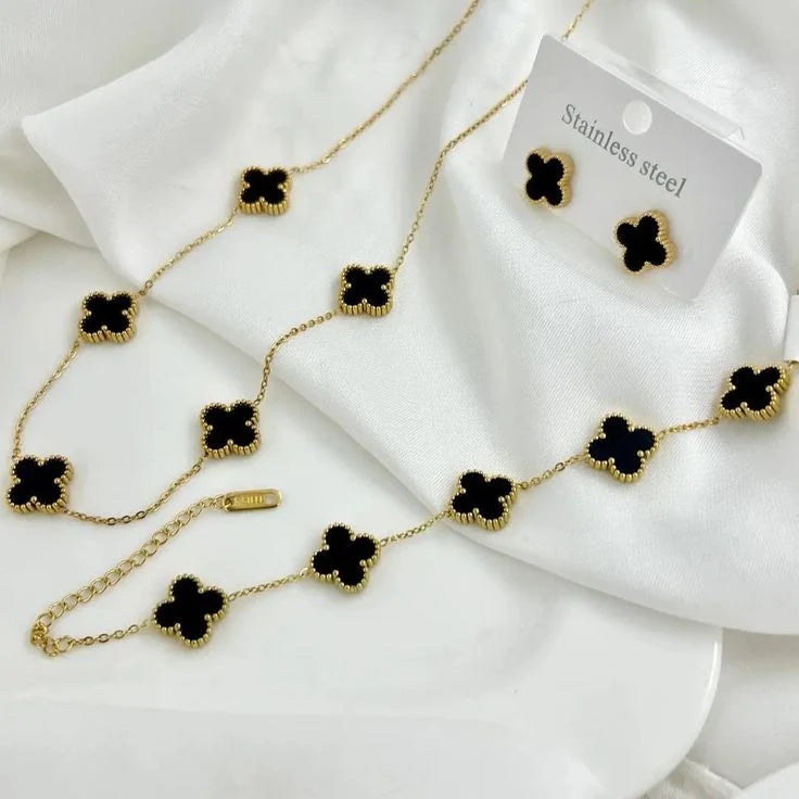 Gold necklace with black clover-shaped stones on a white fabric background