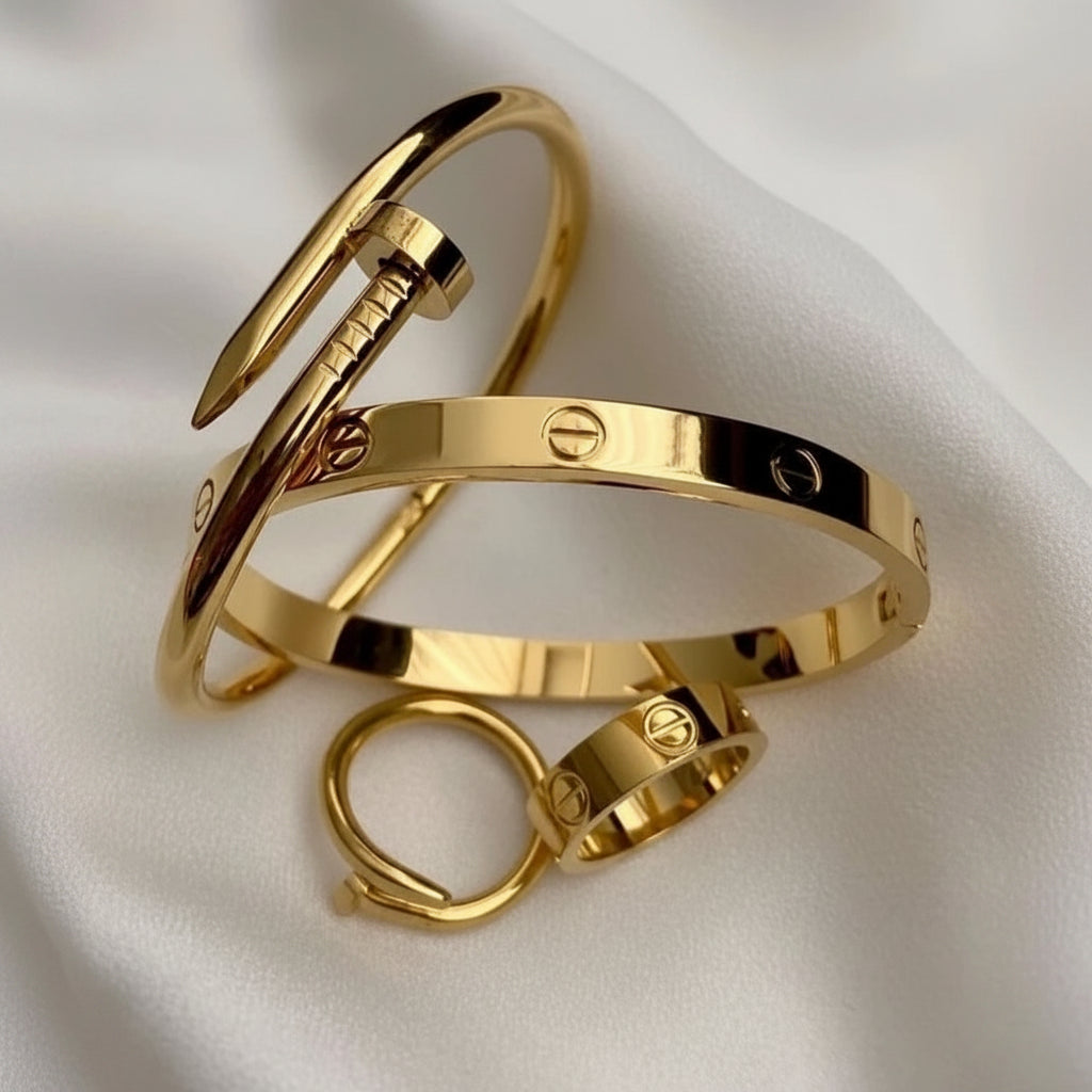 A stack of gold-tone jewelry pieces, including a screw-ring bangle and a screw-hinge ring, displayed on a soft white fabric background.