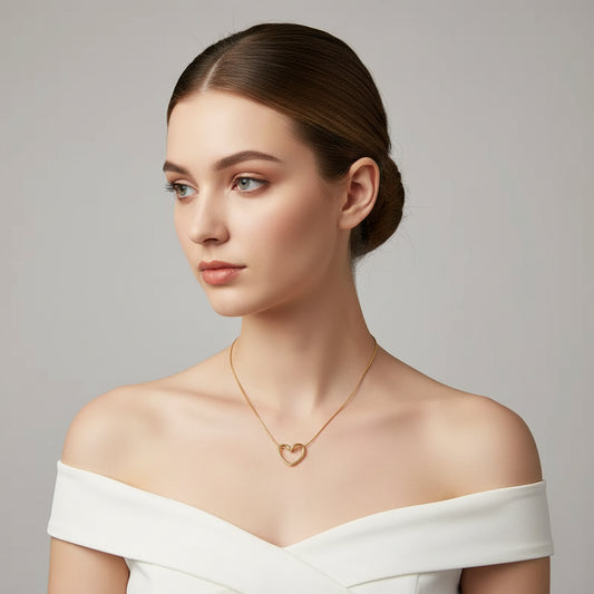 A delicate gold chain necklace with a small open heart pendant, resting on a white ceramic dish against a dark background.