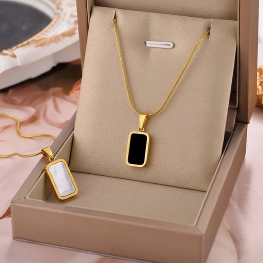 Gold rectangular pendant necklace with a black center, displayed in a beige jewelry box with an inset close-up of the pendant.